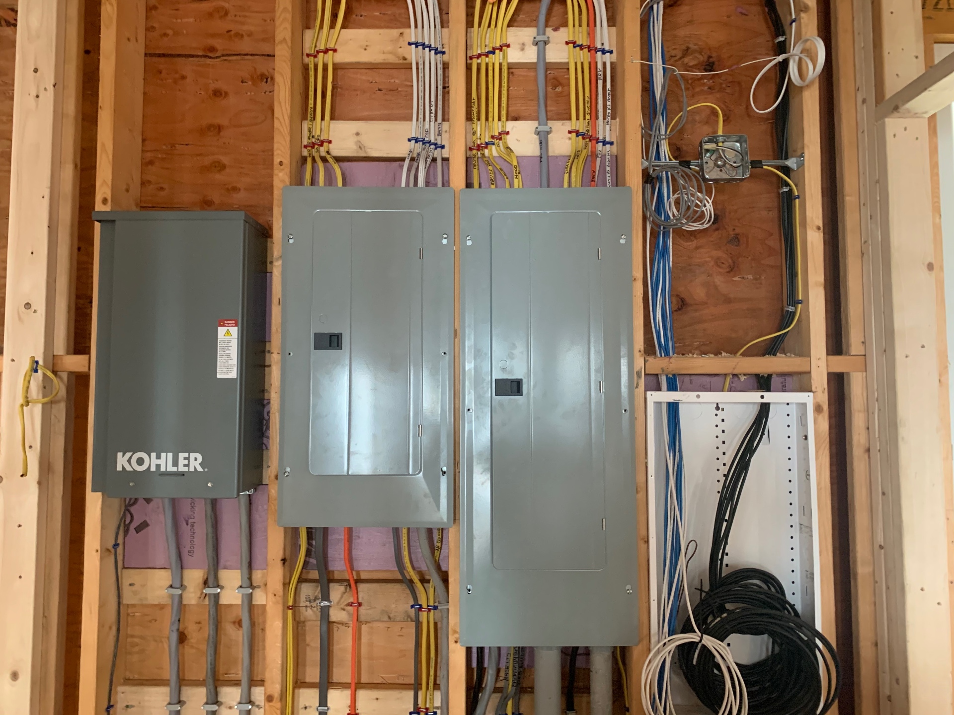 Twin service panels with Kohler standby generator transfer switch installed by Andrew